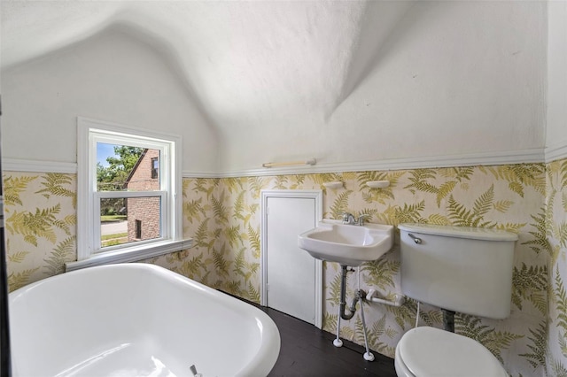 bathroom with toilet, wallpapered walls, a freestanding tub, and vaulted ceiling