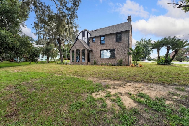 view of front of house with a shingled roof, brick siding, a chimney, and a front lawn