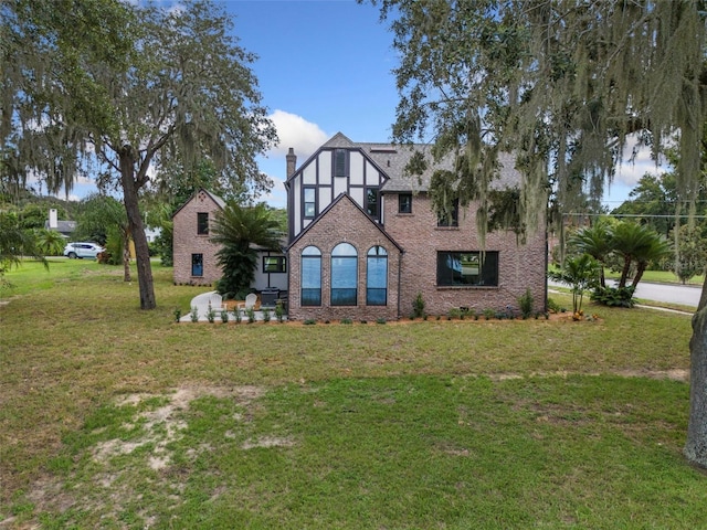 tudor home with a front lawn, a chimney, and brick siding