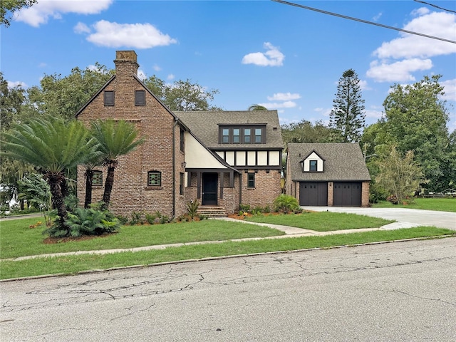 tudor-style house featuring a front yard, brick siding, driveway, and an attached garage