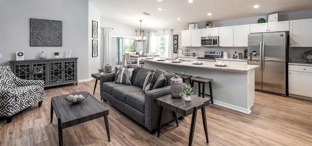 living room featuring lofted ceiling, light hardwood / wood-style flooring, sink, and an inviting chandelier