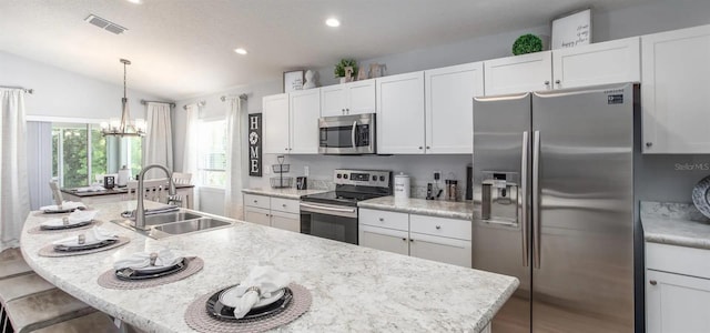 kitchen with lofted ceiling, an island with sink, hanging light fixtures, appliances with stainless steel finishes, and sink