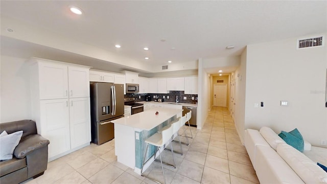 kitchen with a breakfast bar area, appliances with stainless steel finishes, backsplash, white cabinets, and a kitchen island