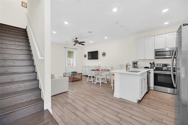 kitchen with kitchen peninsula, ceiling fan, light hardwood / wood-style floors, appliances with stainless steel finishes, and sink