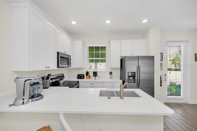 kitchen with light hardwood / wood-style flooring, kitchen peninsula, white cabinets, appliances with stainless steel finishes, and sink