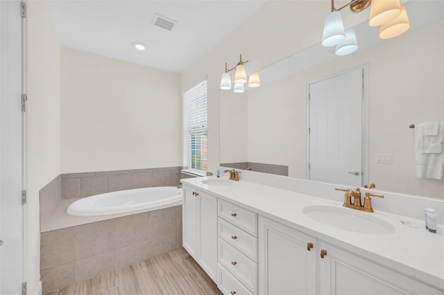 bathroom featuring a relaxing tiled tub, wood-type flooring, and double sink vanity