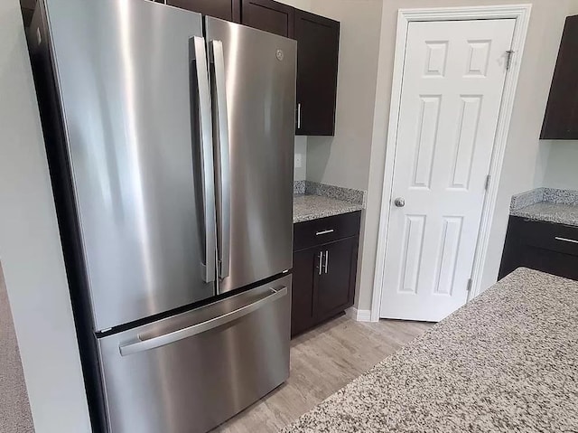 kitchen with light stone counters, dark brown cabinets, stainless steel fridge, and light hardwood / wood-style flooring