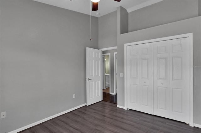 unfurnished bedroom featuring a towering ceiling, dark hardwood / wood-style floors, ceiling fan, and a closet