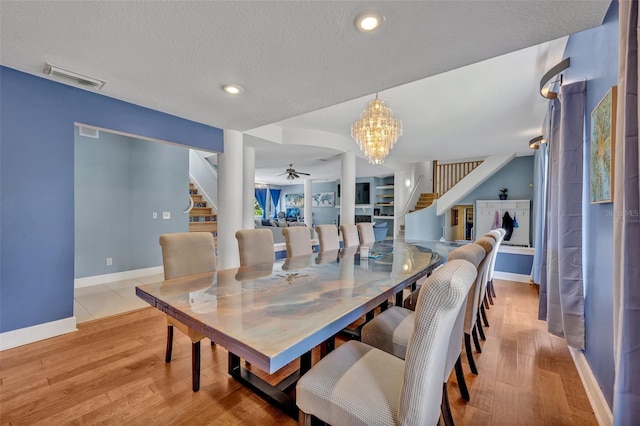 dining area with a textured ceiling, ceiling fan with notable chandelier, light wood-type flooring, and built in shelves