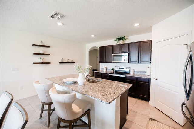 kitchen featuring a breakfast bar area, a center island with sink, dark brown cabinetry, appliances with stainless steel finishes, and light tile patterned floors