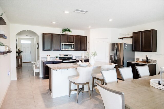 kitchen with dark brown cabinetry, appliances with stainless steel finishes, a breakfast bar area, and a center island with sink