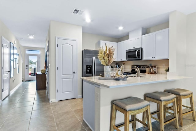 kitchen featuring light tile patterned floors, a kitchen bar, kitchen peninsula, stainless steel appliances, and white cabinets