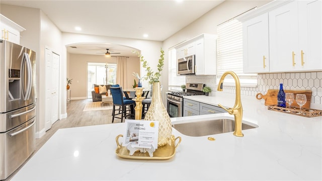 kitchen featuring white cabinetry, ceiling fan, stainless steel appliances, light stone counters, and sink