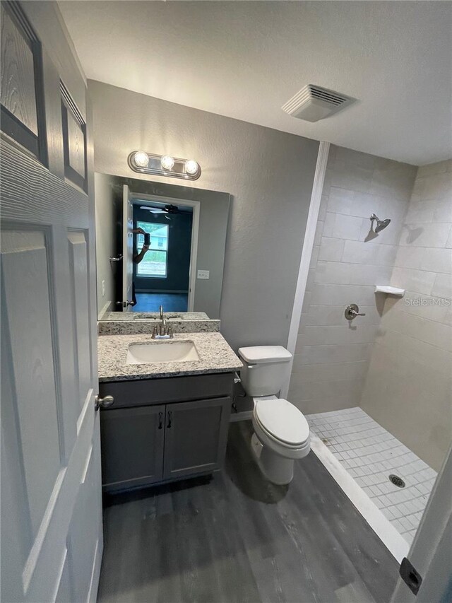 bathroom with a tile shower, toilet, vanity, and hardwood / wood-style flooring