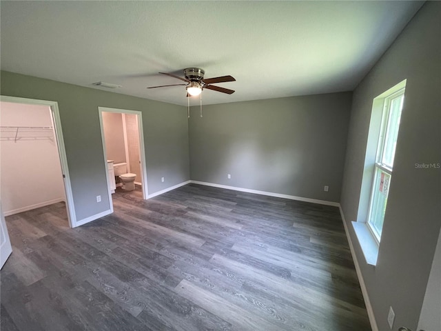 unfurnished bedroom featuring dark wood-type flooring, ensuite bathroom, a spacious closet, a closet, and ceiling fan