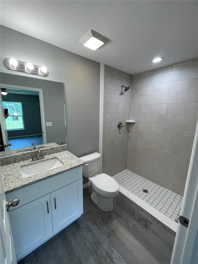 full bathroom with a textured ceiling, toilet, wood finished floors, vanity, and tiled shower