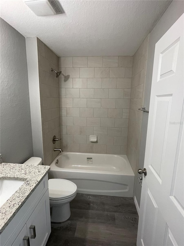 full bathroom with hardwood / wood-style floors, vanity, a textured ceiling, toilet, and tiled shower / bath