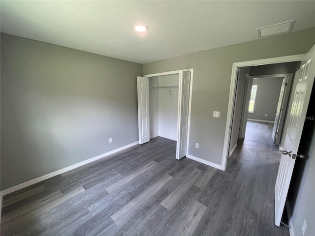 unfurnished bedroom with dark wood-style floors, baseboards, visible vents, and a closet