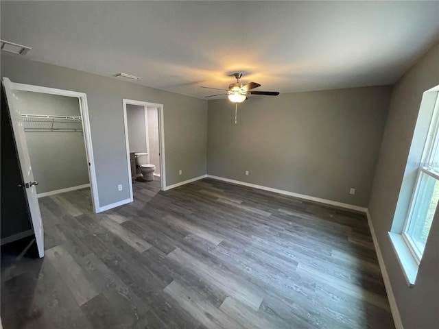 unfurnished bedroom with dark wood-type flooring, ensuite bathroom, a walk in closet, a closet, and ceiling fan