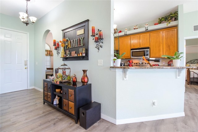 kitchen with an inviting chandelier, light hardwood / wood-style flooring, light stone counters, and kitchen peninsula