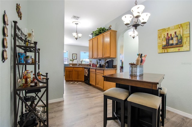 kitchen with black dishwasher, sink, pendant lighting, light wood-type flooring, and a chandelier