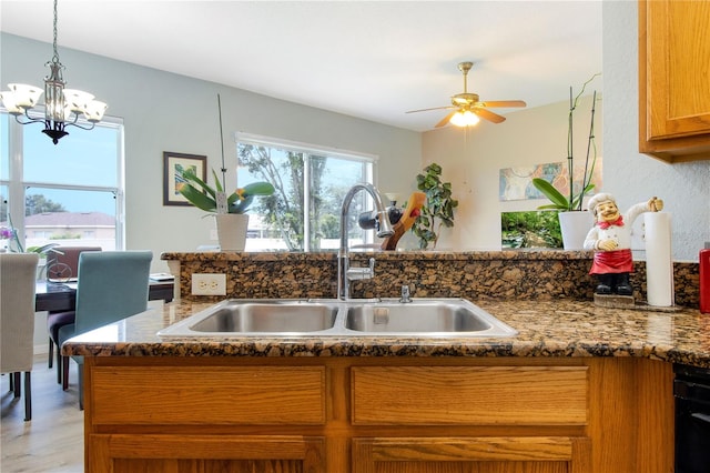 kitchen featuring dark stone countertops, kitchen peninsula, ceiling fan with notable chandelier, light hardwood / wood-style floors, and sink