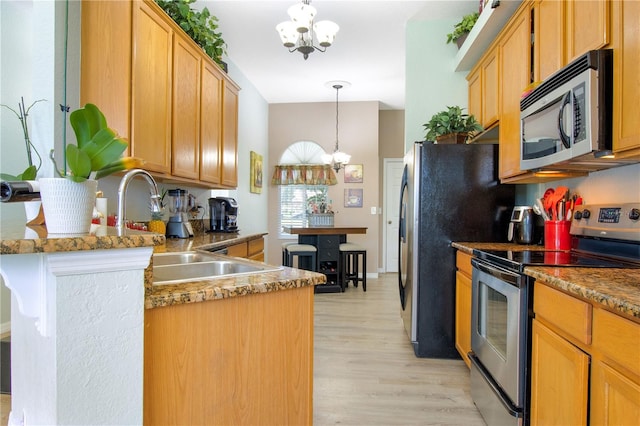 kitchen featuring appliances with stainless steel finishes, light hardwood / wood-style flooring, an inviting chandelier, sink, and decorative light fixtures