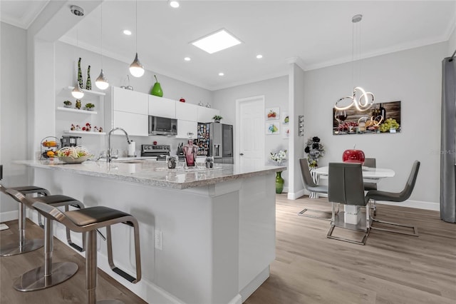 kitchen featuring white cabinetry, light hardwood / wood-style flooring, stainless steel appliances, light stone countertops, and pendant lighting