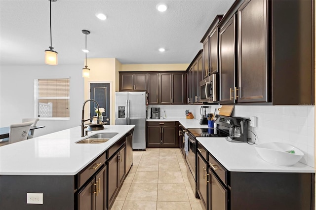 kitchen featuring light tile patterned floors, sink, hanging light fixtures, stainless steel appliances, and a center island with sink