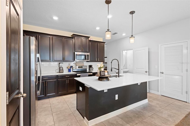 kitchen with sink, light tile patterned floors, appliances with stainless steel finishes, pendant lighting, and a kitchen island with sink