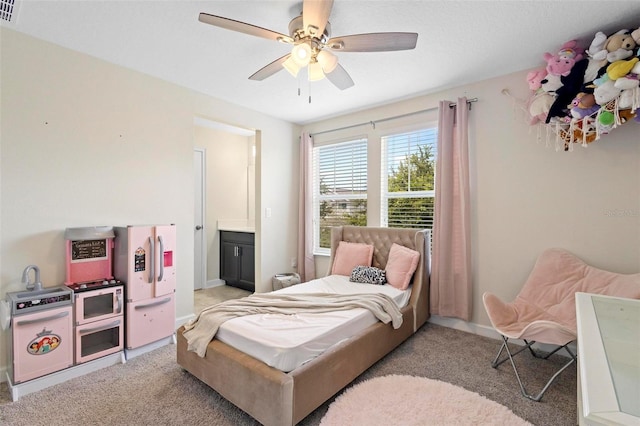 bedroom featuring ceiling fan, light colored carpet, white refrigerator with ice dispenser, and ensuite bath