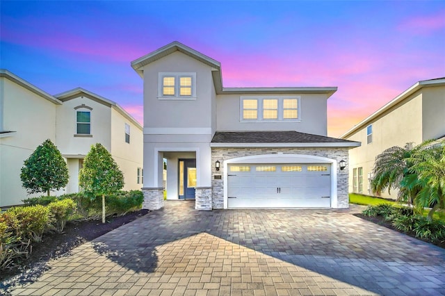 view of front of house with stone siding, decorative driveway, stucco siding, and an attached garage