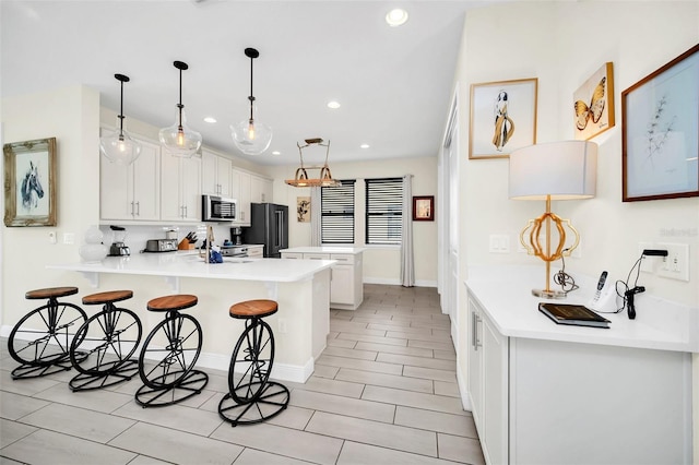 kitchen with a kitchen breakfast bar, white cabinetry, stainless steel microwave, freestanding refrigerator, and a peninsula