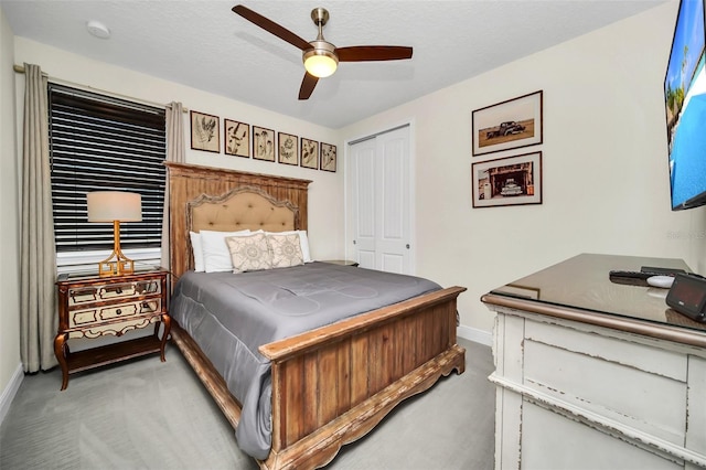 bedroom with a closet, a textured ceiling, baseboards, a ceiling fan, and light carpet