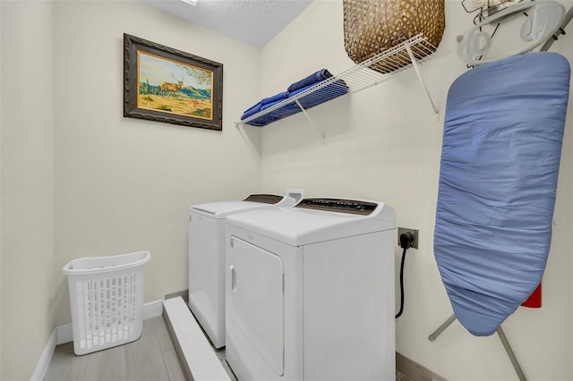 washroom featuring a textured ceiling, baseboards, wood finished floors, laundry area, and washing machine and dryer