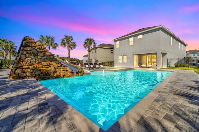 pool at dusk featuring fence, a water slide, a patio area, and a fenced in pool