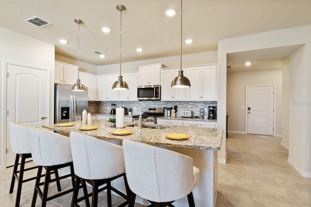 kitchen featuring stainless steel appliances, pendant lighting, a breakfast bar, and an island with sink