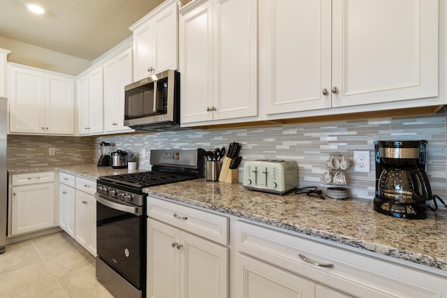 kitchen with appliances with stainless steel finishes, light tile patterned floors, decorative backsplash, light stone countertops, and white cabinetry