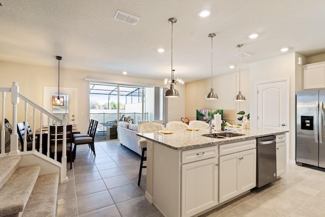 kitchen featuring appliances with stainless steel finishes, white cabinets, a center island with sink, sink, and decorative light fixtures