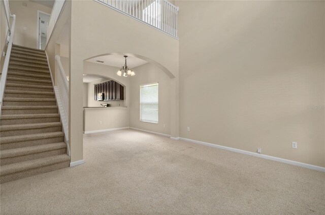 unfurnished living room with a high ceiling, carpet, and a notable chandelier