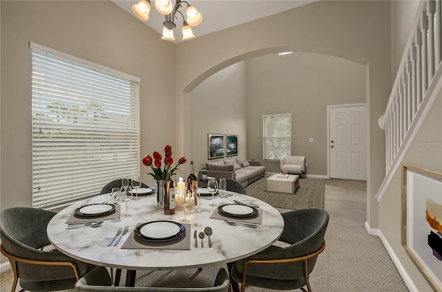 carpeted dining area with a towering ceiling and a notable chandelier