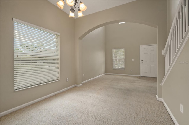 carpeted empty room featuring an inviting chandelier and a high ceiling