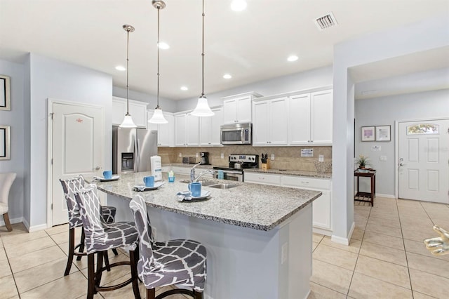 kitchen with pendant lighting, white cabinetry, sink, stainless steel appliances, and a center island with sink