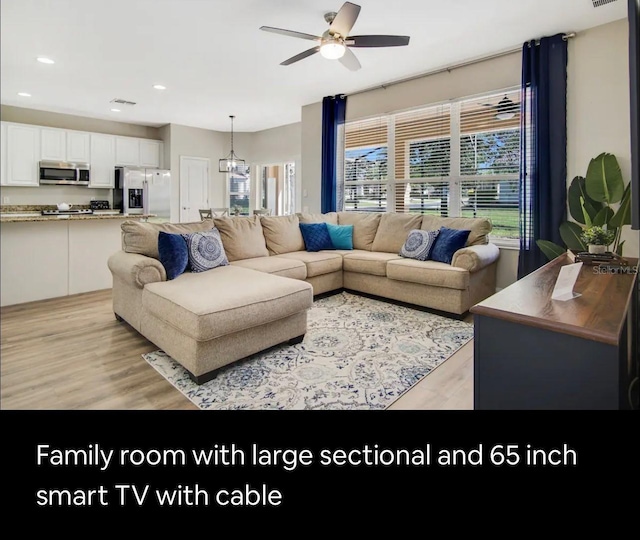 living room with ceiling fan with notable chandelier and light hardwood / wood-style flooring