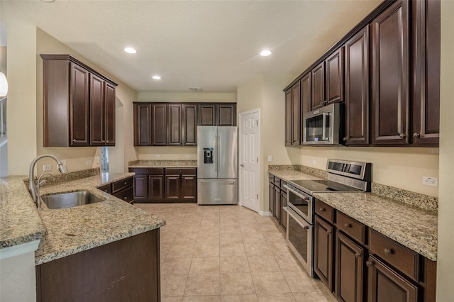 kitchen with sink, dark brown cabinetry, appliances with stainless steel finishes, light tile patterned floors, and light stone counters