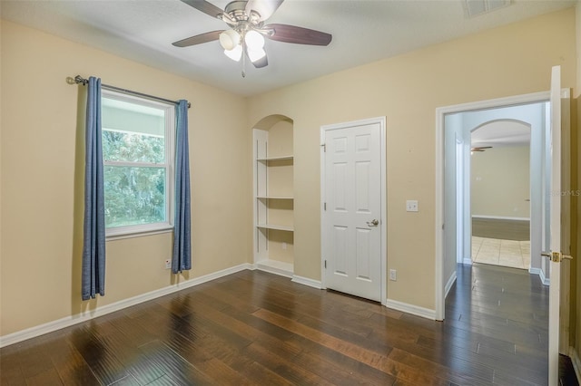 unfurnished room featuring ceiling fan, dark wood-type flooring, and built in shelves