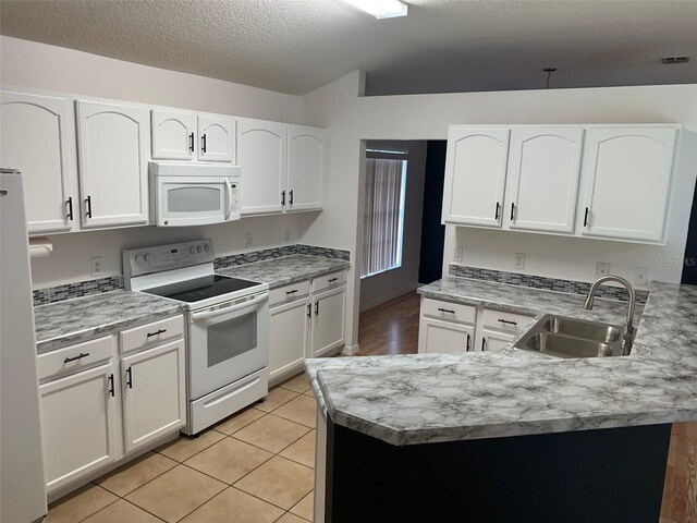 kitchen with sink, white appliances, light tile patterned floors, kitchen peninsula, and white cabinets