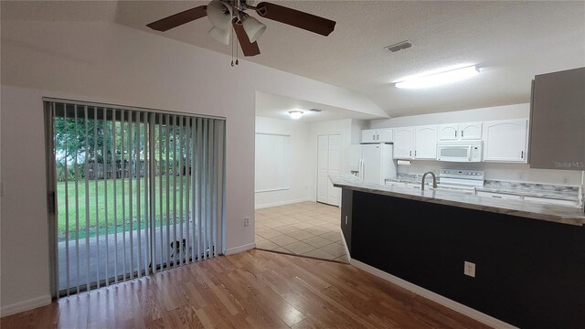 kitchen with vaulted ceiling, white cabinetry, light tile patterned flooring, and white appliances