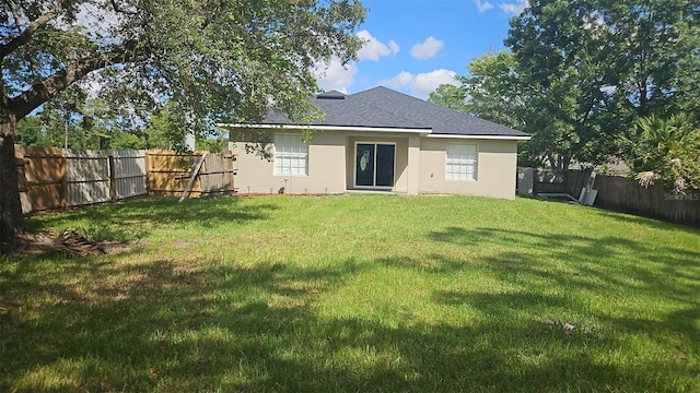 rear view of house featuring roof with shingles, a lawn, a fenced backyard, and stucco siding