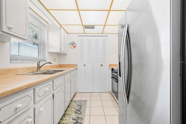 kitchen featuring light tile patterned floors, sink, range, and stainless steel refrigerator